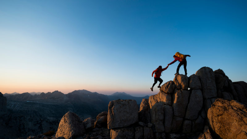 Deux personnes s'aidant à gravir une montagne