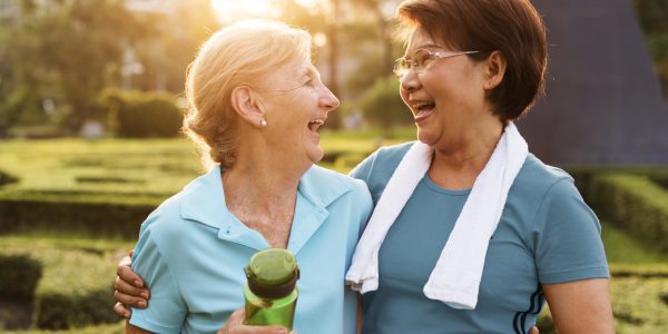 Deux femmes seniors rigolant après avoir fait du sport, l'une avec une serviette et l'autre avec une gourde à la main