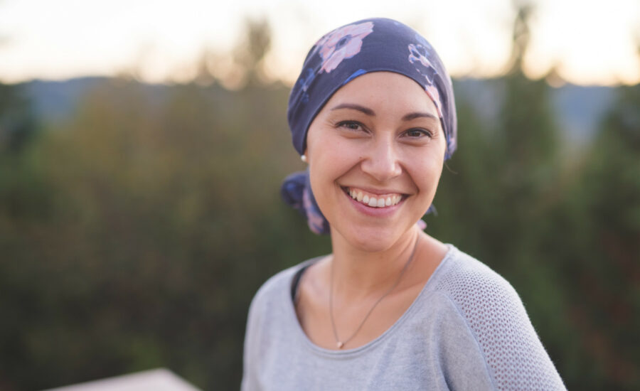 Une femme atteinte d'un cancer avec un bandana sur la tête regardant l'objectif en souriant - soutien maladies graves